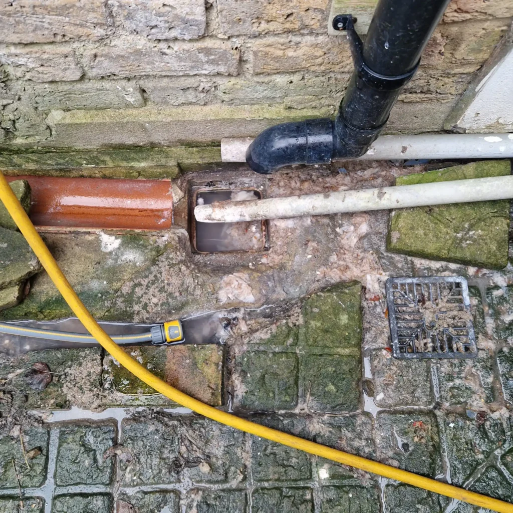 Blocked outside drain overflowing with dirty water and silt in a Sutton garden