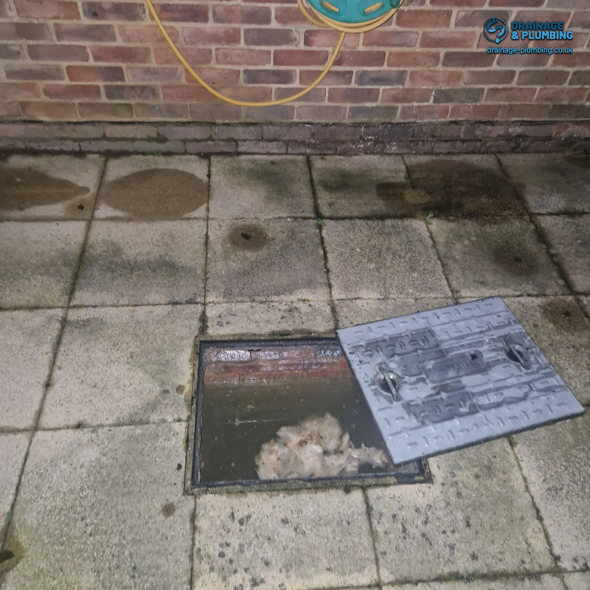 Local drain specialist inspecting a manhole cover on a residential street in South East England