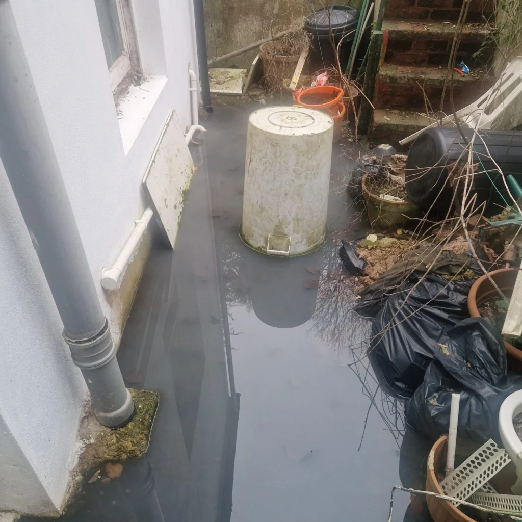 A blocked outdoor drain gully affected by grease, food residue, and general debris, often linked to kitchen wastewater.