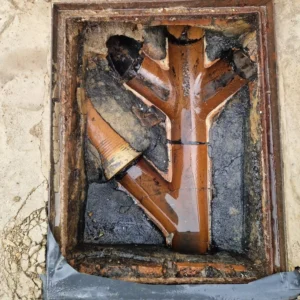 Professional drain unblocker inspecting an open manhole and blocked drainage pipes