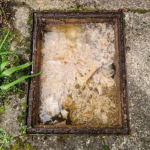 Professional drain unblocker inspecting an overflowing blocked outside drain and manhole.