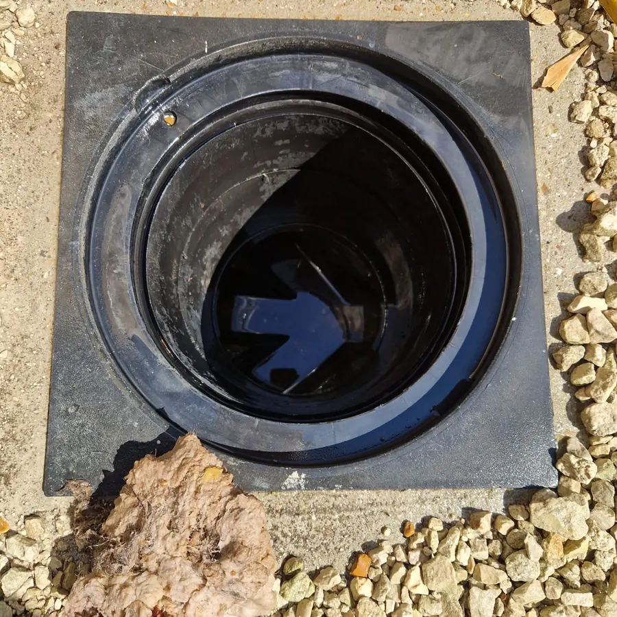 The same inspection chamber after clearing, empty and dry with the plastic channel visible and the fat mass lifted out onto the slab beside it