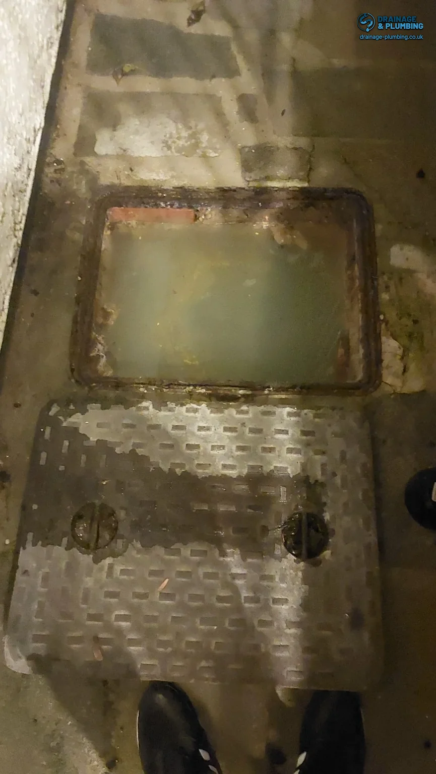 Open inspection chamber filled with murky water, with the cover resting beside it